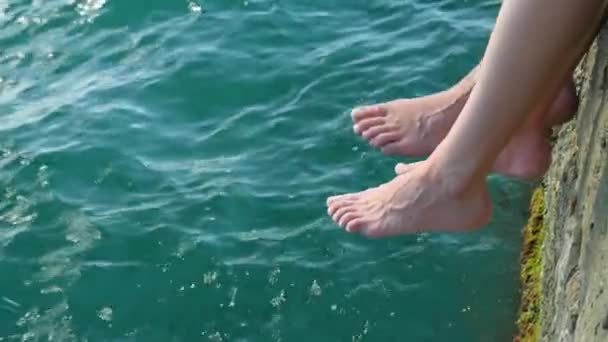 Un couple assis sur la jetée et mouille les pieds dans la mer. 4k, au ralenti — Video