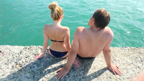 Una pareja sentada en el muelle y moja los pies en el mar. 4k, cámara lenta — Vídeos de Stock
