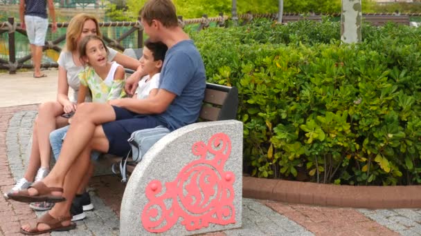 Familia feliz sentarse en un banco en un parque de atracciones y divertirse. 4k. espacio de copia. estilo de vida. Movimiento lento — Vídeos de Stock