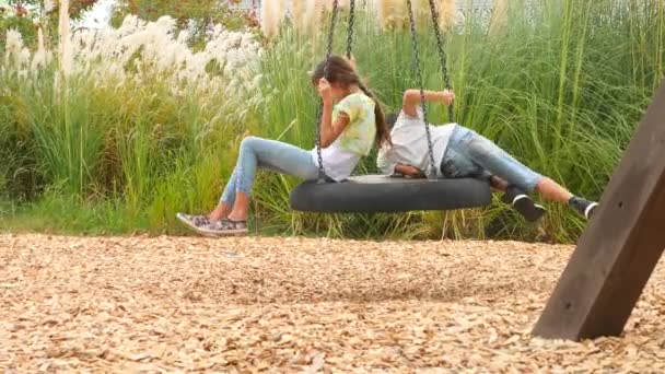 Irmão feliz e irmã balançando em um balanço no parque de diversões na cidade. 4K, espaço de cópia, câmera lenta. estilo de vida — Vídeo de Stock