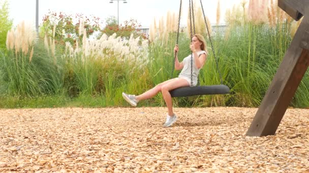 Romantic young woman swinging on a swing on the amusement park in the city. 4k, copy space. Slow motion. — Stock Video