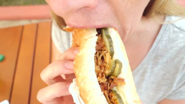 Atrakcyjna dziewczyna zjada świeże pitę z sałatką z warzyw i mięsa, siedząc w kawiarni fast food pod drzewem w parku. 4 k zwolnionym tempie — Wideo stockowe
