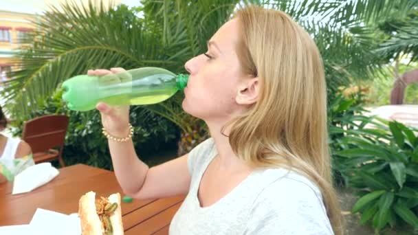 Una ragazza attraente mangia pane fresco pita con un'insalata di verdure fresche e carne, seduto in un fast food caffè sotto un albero nel parco. 4K rallentatore — Video Stock