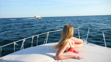 Çekici kadın denizde bir yaz gününde bir yatta. ince busty sarışın uzun saçlı, güneş gözlüğü ve parlak kırmızı bikini giyen açık denizde bir teknenin güvertesinde güneşlenirken. ağır çekim
