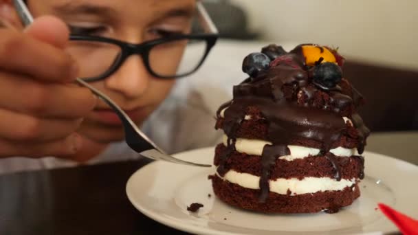 Мальчик в очках ест вкусный десерт в кафе. 4k slow motion — стоковое видео