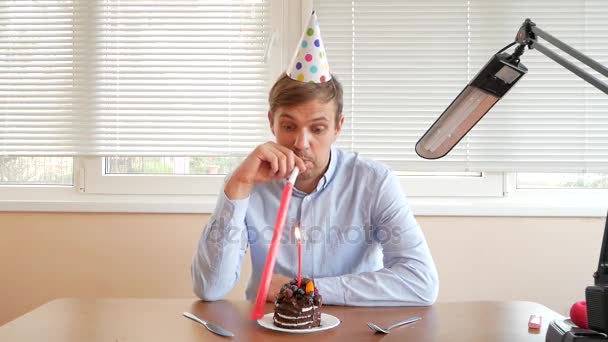 Um homem solitário celebra um feriado, ele se senta sozinho em uma mesa com um bolo e uma vela . — Vídeo de Stock