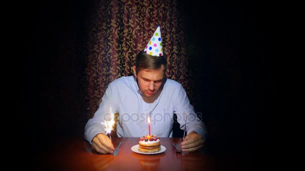 Een eenzame man een vakantie viert, hij zit alleen aan een tafel met een taart en een kaars. 4k, slow-motion — Stockvideo