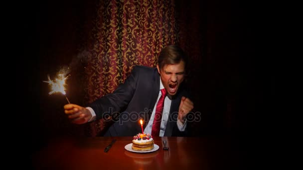 Um homem solitário celebra um feriado, ele se senta sozinho em uma mesa com um bolo e uma vela. 4k, câmera lenta — Vídeo de Stock