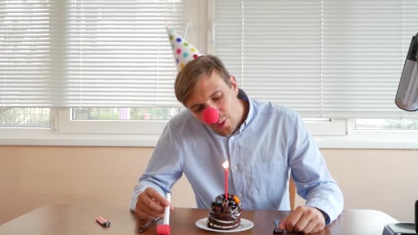 Um homem solitário celebra um feriado, ele se senta sozinho em uma mesa com um bolo e uma vela . — Vídeo de Stock