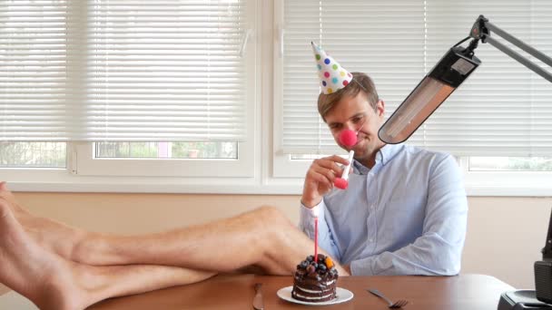 A lone man celebrates a holiday, he sits alone at a table with a cake and a candle. — Stock Video