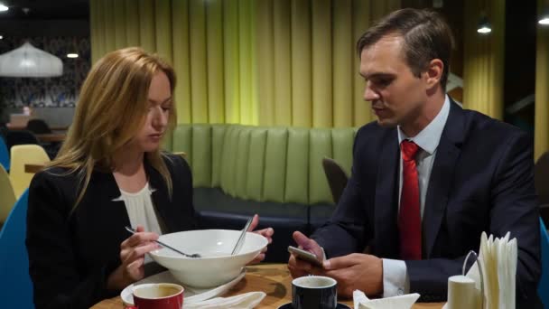 ビジネス パートナーの男性と女性は、カフェ利用のスマート フォンで昼食をとる。4 k コピー スペース — ストック動画