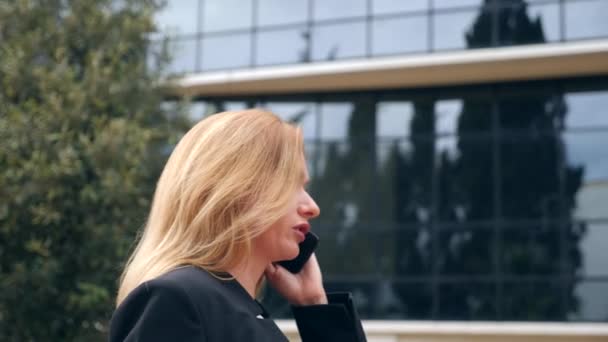 Business woman in a business suit with a smartphone, walking on a business center, walking in the city, steadicam shot. 4k, slow motion, copy space — Stock Video