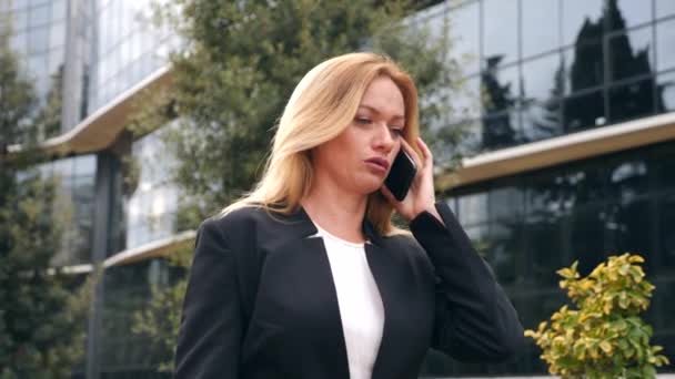 Donna d'affari in giacca e cravatta con uno smartphone, camminare su un business center, camminare in città, colpo steadicam. 4k, rallentatore, spazio di copia — Video Stock