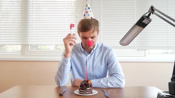 A lone man celebrates a holiday, he sits alone at a table with a cake and a candle. — Stock Video