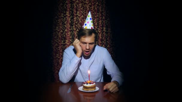 Un hombre solitario celebra una fiesta, se sienta solo en una mesa con un pastel y una vela. 4k, cámara lenta — Vídeos de Stock