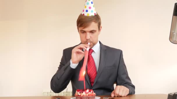 Одинокий человек празднует праздник, он сидит один за столом с тортом и свечой. 4k, slow motion — стоковое видео