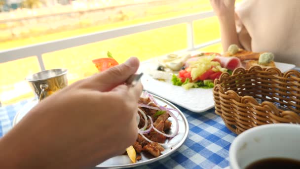 Ein romantisches Paar, das in einem Café im Freien griechische Gerichte, Souvlaki und ein griechisches Frühstück isst. 4k, Zeitlupe — Stockvideo