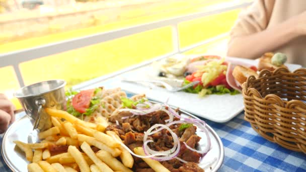 Una pareja romántica comiendo en un café al aire libre platos griegos, souvlaki y un desayuno griego. 4k, cámara lenta — Vídeos de Stock