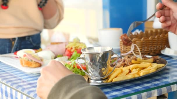Um casal romântico comendo em um café ao ar livre pratos gregos, souvlaki e um café da manhã grego. 4k, câmera lenta — Vídeo de Stock