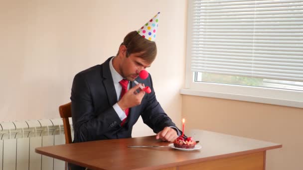 Un hombre solitario celebra una fiesta, se sienta solo en una mesa con un pastel y una vela. 4k, cámara lenta — Vídeos de Stock