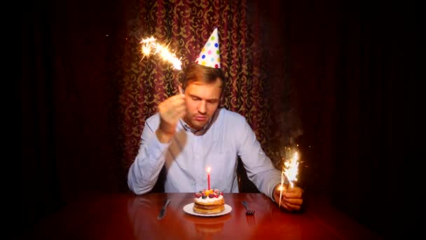 Un hombre solitario celebra una fiesta, se sienta solo en una mesa con un pastel y una vela. 4k, cámara lenta — Vídeos de Stock