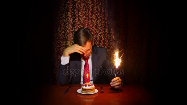 Одинокий человек празднует праздник, он сидит один за столом с тортом и свечой. 4k, slow motion — стоковое видео