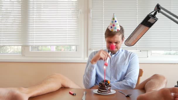 Um homem solitário celebra um feriado, ele se senta sozinho em uma mesa com um bolo e uma vela. 4k, câmera lenta — Vídeo de Stock