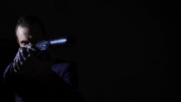 Человек вытаскивает пистолет в темноте и целится в камеру. 4k, slow motion — стоковое видео