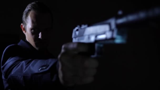 Чоловік витягує пістолет у темряві і прицілюється до камери. 4k, повільний рух — стокове відео