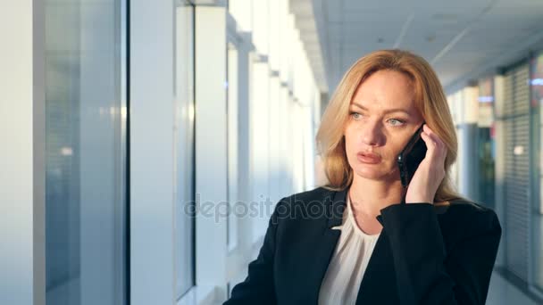 Business woman in a business suit with a smartphone, walking along the corridor of the business center with panoramic windows, 4k, slow motion, space for copying — Stock Video