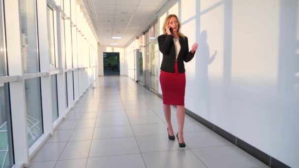 Zakenvrouw in een bedrijf passen met een smartphone, wandelen langs de corridor van het business center met panoramische ramen, 4k, langzame beweging, ruimte voor kopiëren — Stockvideo