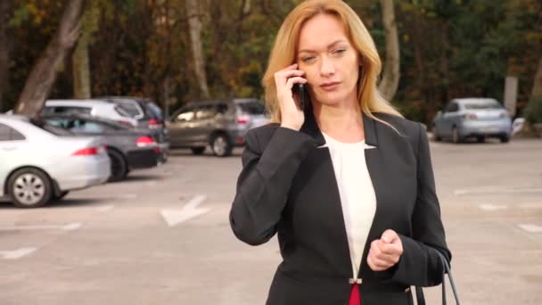 Donna d'affari in giacca e cravatta con uno smartphone, camminare su un business center, camminare in città, colpo steadicam. 4k, rallentatore, spazio di copia — Video Stock