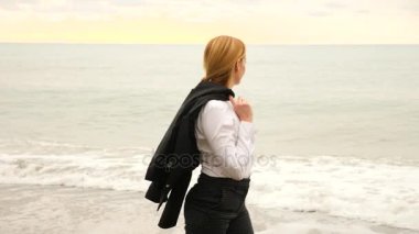 İşkadını takım ayakta sahilde. Deniz Manzaralı seviyor. 4k, ağır çekim. o onun ceketini alır