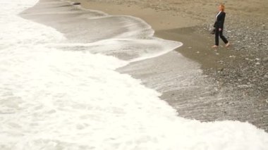 İşkadını takım ayakta sahilde. Deniz Manzaralı seviyor. 4k, ağır çekim. o onun yüksek topuklu alır ve suya gider