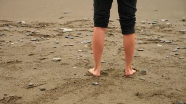 Femme d'affaires en costume debout sur la plage. elle aime la vue sur la mer. 4k, au ralenti. pieds en vagues gros plan — Video