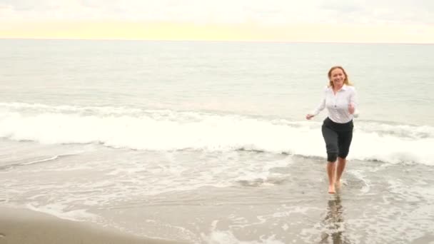 Businessman in suit on the beach. she runs away from the wave. 4k, slow motion — Stock Video