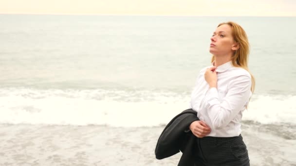 Businesswoman in suit standing on beach. she enjoys the sea view. 4k, slow motion. she unfastened her shirt and inhales the sea air — Stock Video