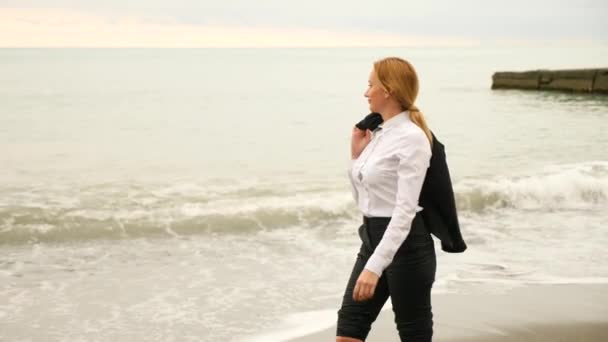 Businesswoman in suit standing on beach. she enjoys the sea view. 4k, slow motion. she takes off her jacket — Stock Video