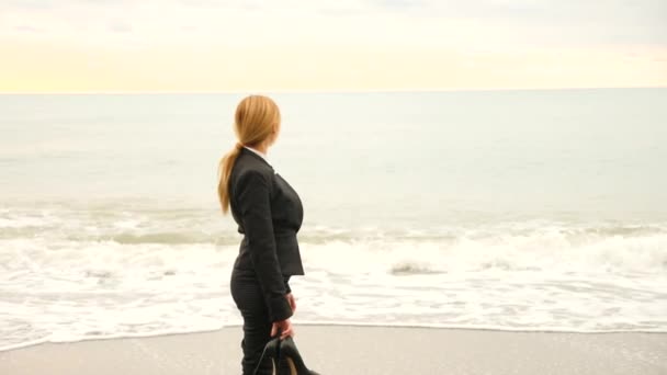 Бизнесмен в костюме стоит на пляже. Ей нравится вид на море. 4k, slow motion . — стоковое видео