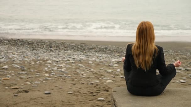 Деловая женщина в костюме на пляже. сидя в позе лотоса и медитируя у моря. 4k, slow motion — стоковое видео