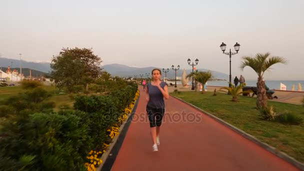 Corredor de camino mujer corriendo en el parque, trotando a lo largo del palmeral, corriendo mujer al aire libre, Parque con palmeras, terraplén, verano. 4k cámara lenta — Vídeo de stock