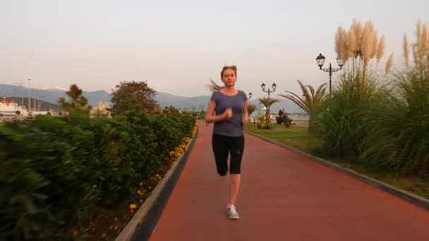 Road runner vrouw uitgevoerd in park, joggen langs de palmentuin, Running vrouw buitenshuis, Park met palmbomen, embankment, zomer. 4 k slow-motion — Stockvideo