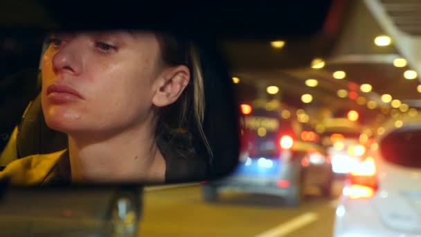 Riflessione di un volto femminile con gli occhi azzurri nello specchio retrovisore, donna al volante di notte, luci notturne della città offuscate e fari dell'auto. 4k, rallentatore — Video Stock