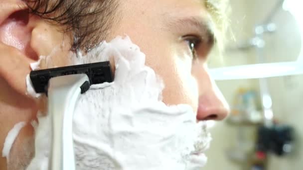 Человек бреет лицо. красивый мужчина бреется в ванной. 4К, замедленная съемка. макро — стоковое видео