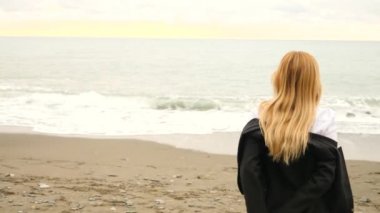 İşkadını takım ayakta sahilde. Deniz Manzaralı seviyor. 4k, ağır çekim. o onun ceketini alır