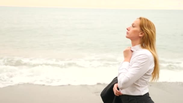 Businesswoman in suit standing on beach. she enjoys the sea view. 4k, slow motion. she unfastened her shirt and inhales the sea air — Stock Video