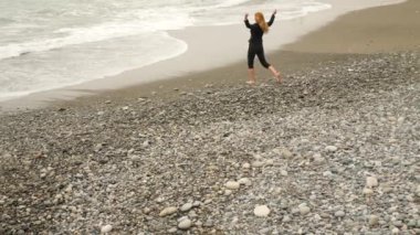 İşkadını takım ayakta sahilde. Deniz Manzaralı seviyor. 4k, ağır çekim. o onun yüksek topuklu alır ve suya gider