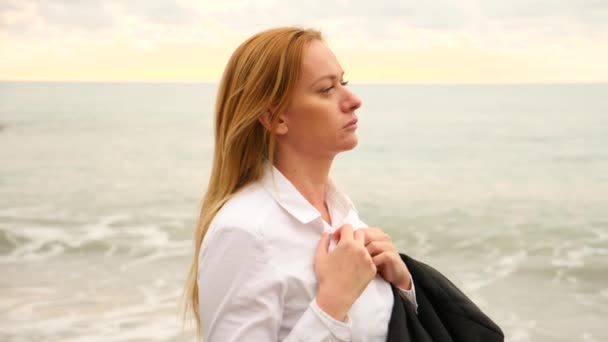 Donna d'affari in giacca e cravatta in piedi sulla spiaggia. si gode la vista sul mare. 4k, rallenta. si slacciò la camicia e inalò l'aria di mare — Video Stock