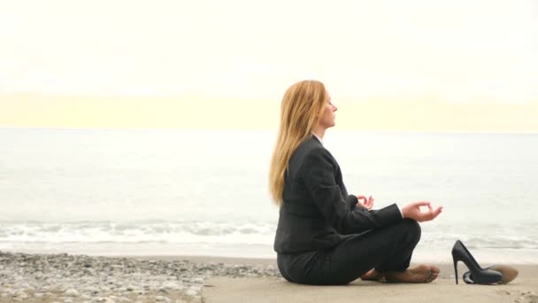 Affärskvinna i kostym på stranden. sitter i lotusställning och meditera vid havet. 4k, Slowmotion — Stockvideo