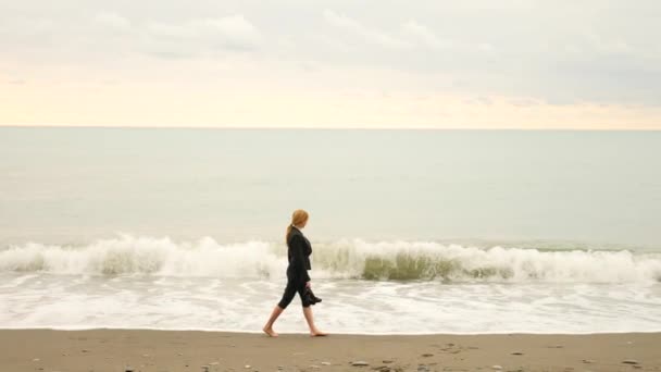 Podnikatelka v obleku, stojící na pláži. Ona má výhled na moře. 4k, zpomalené. nohy ve vlnách zblízka — Stock video